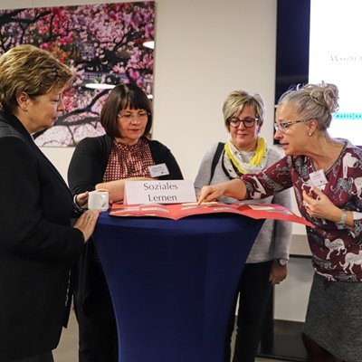 Vier Frauen stehen um einen Tisch eine zeigt auf etwas