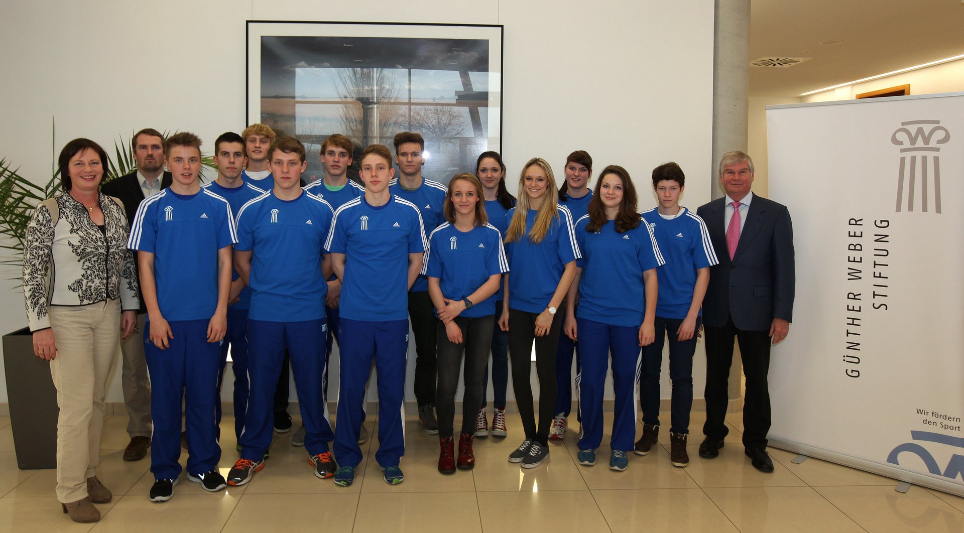 Eine Gruppe posiert in Vereinsfarben neben einem Banner der Stiftung und dem Stiftungsgründer 