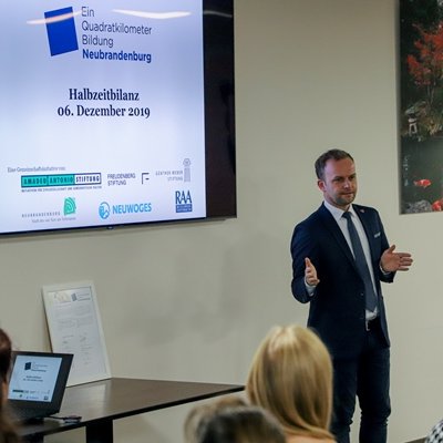 Ein Mann im Anzug steht vor einer Gruppe, im Hintergrund sieht man einer Powerpoint Folie